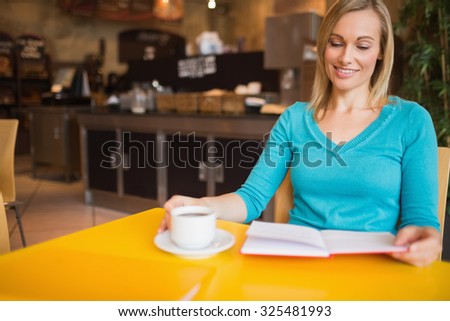 Young woman holding book with coffee cup on table at cafe
