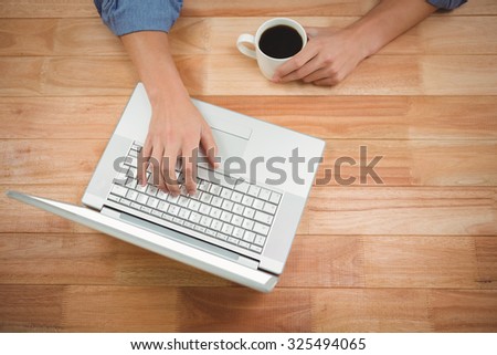 Man holding coffee while working on laptop at desk in office