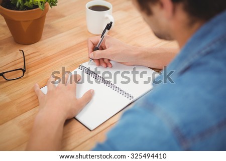 Cropped image of hipster writing on spiral book at desk in office