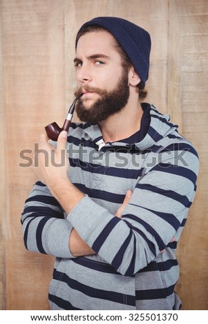 Portrait of serious hipster smoking pipe against wooden wall