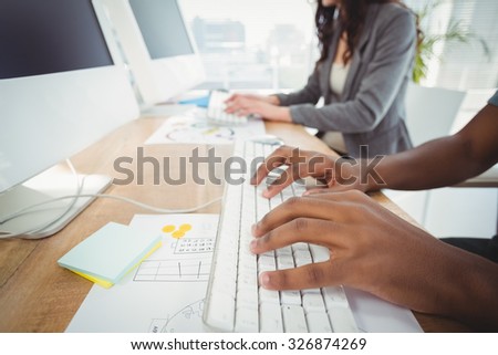 Cropped hands typing on keyboard at computer desk with coworker in office