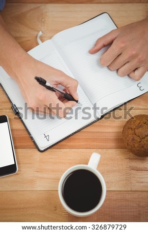 Cropped image of man writing on diary with muffin and coffee at desk in office