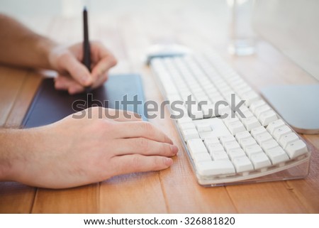 Cropped hand of man using graphics tablet at computer desk in office