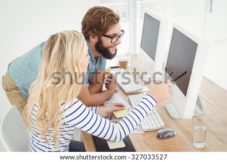 High angle view of woman pointing at computer with stylus while sitting by man in creative office
