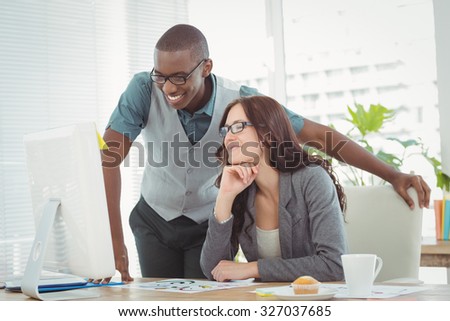 Smiling business professionals looking at computer while working at desk in office