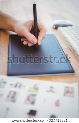 Cropped hand of man drawing on graphics tablet at desk in office
