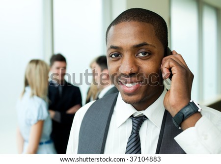 Ethnic businessman on phone in office with his team in the background