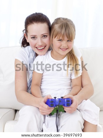 Smiling mother and daughter playing video games at home