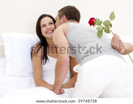 Husband giving a rose and a kiss to his beautiful wife in bed