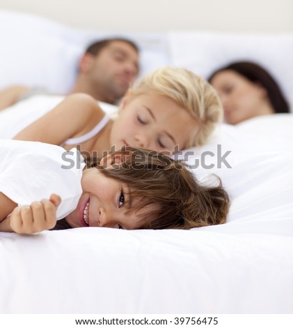 Little boy smiling on bed wile his parents and sister sleep