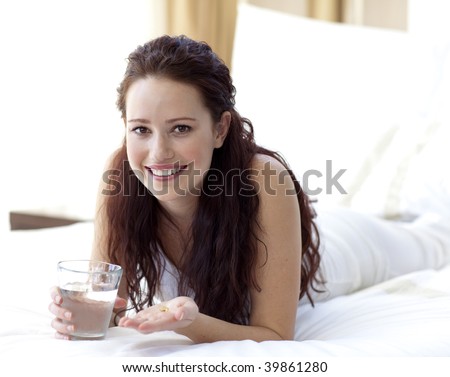 Smiling woman in bed taking pills with water