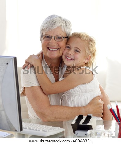 Granddaughter and grandmother hugging and using a computer at home
