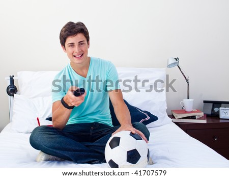 Teen guy watching a football match in television in his bedroom