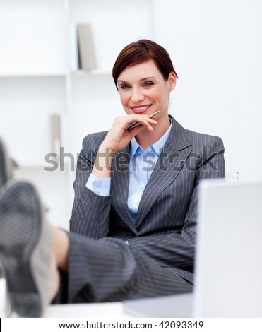 Attractive businesswoman leaning feet on desk and smiling at the camera