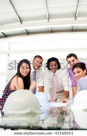 Architects smiling at the camera in a meeting with hardhats on the table