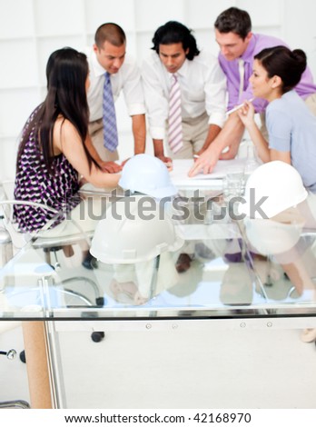 A group of architects studying plans in a meeting with hardhats on the table