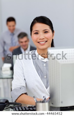 Charming asian businesswoman working at a computer with her colleagues in the background