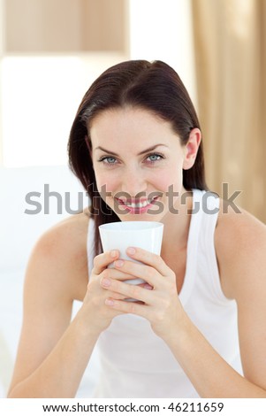 Bright woman drinking a coffee sitting on her bed