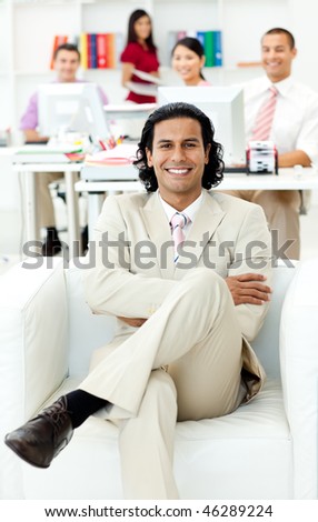 Ethnic manager sitting with his team in the background in the office