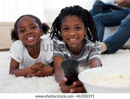 Afro american children watching television and eating pop corn in the living room