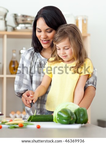 Attentive mother and daughter cutting vegetables together in the kitchen