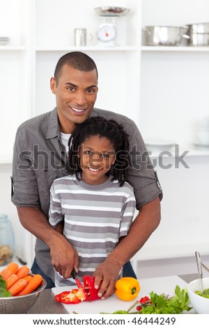Smiling father helping his son cut vegetables in the kitchen