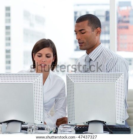 Two business people helping each other with their computers in the office