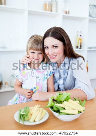 Cute little girl eating vegetables with her mother in the kitchen