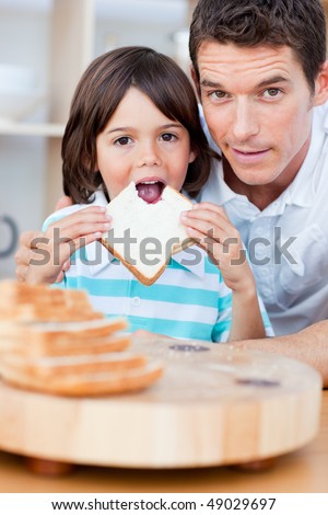 Cute little boy and his father eating bread in the kitchen