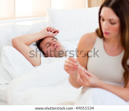 Concerned woman taking her sick husband\'s temperature in their bedroom