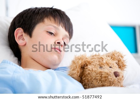 Portrait of a sick boy hugging a teddy bear lying in a hospital bed