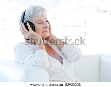 Charming senior woman listening music with headphones sitting on a sofa