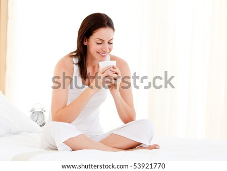 Smiling woman drinking a coffee sitting on her bed at home