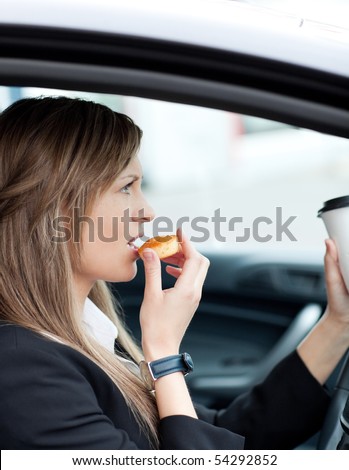 Attractive businesswoman eating and holding a drinking cup while driving to work