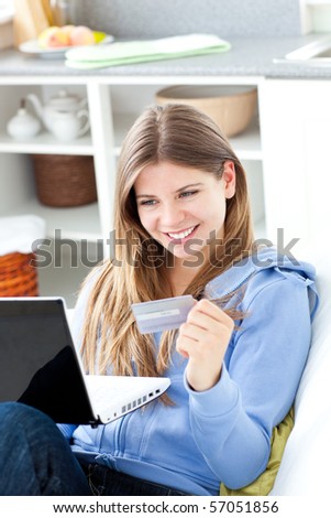 Happy woman with a credit card and a laptop in a kitchen