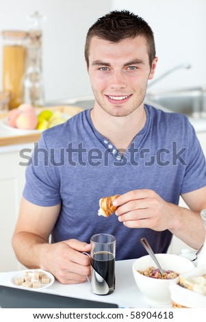 Handsome man eating croissant drinking coffee in the kitchen