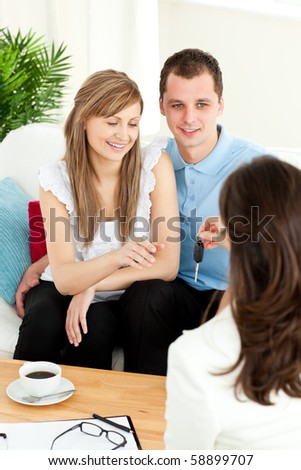 Happy couple receiving new car keys from a female dealer in the living room