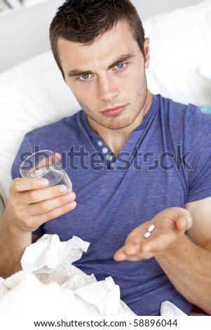 Dejected young man holding pills and water sitting on the sofa looking at the camera