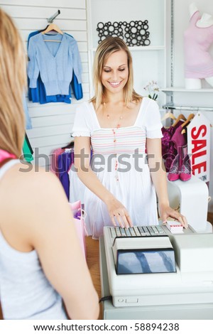 Positive saleswoman standing behind the counter using the cash register in a clothes store