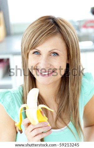 Smiling young holding a banana looking at the camera in the kitchen at home