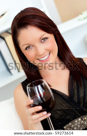 Elegant young woman holding a glass of wine at home looking at the camera