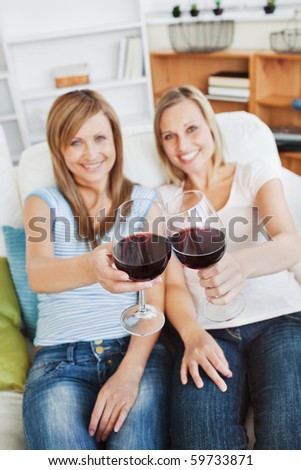 Two bright women holding a wineglass on a sofa at home