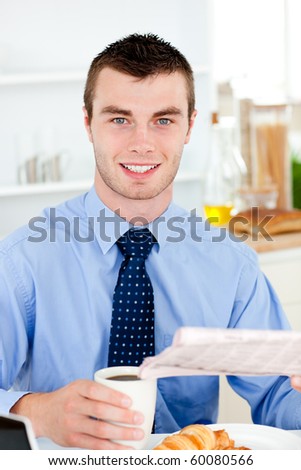 Happy businessman reading the newspaper drinking coffee in the morning at home in the kitchen