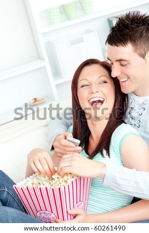 Laughing young couple lying on the sofa with popcorn and remote at home