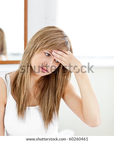 Depressed woman with a headache looking at the camera in the bathroom at home
