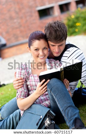 student couple lying on the grass reading a book together at the university campus