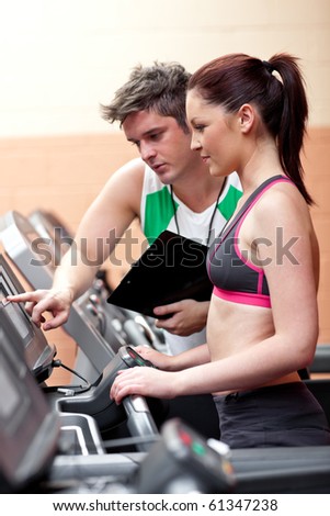 Beautiful female athlete standing on a running machine talking with her personal coach in a fitness center