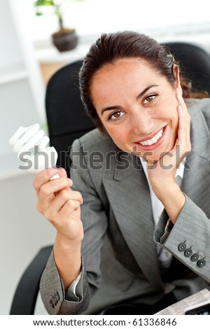 Beautiful businesswoman holding a light bulb in her hand sitting at her desk in her office