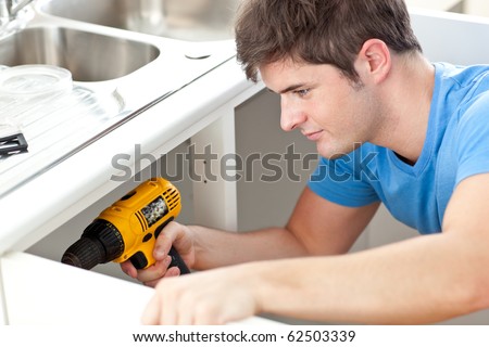 Assertive man holding a drill repairing a kitchen sink at home
