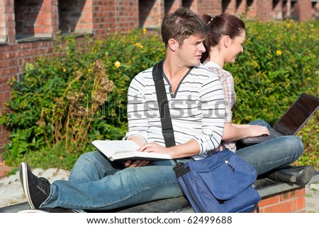Serious couple of students working together with book and laptop in the campus of their university